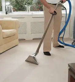Professional carpet cleaner using a hot-water extraction wand and hose machine in a living room in Fort Worth, TX.