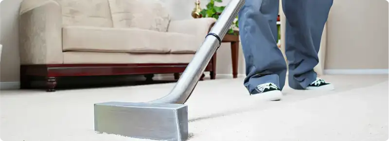 Carpet cleaning technician using a hot-water extraction wand on a light-colored carpet in a living room, Fort Worth, TX.
