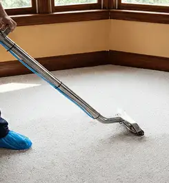Steam carpet cleaning technician using a hot-water extraction wand on a residential carpet, wearing blue protective shoe covers Fort Worth, TX.