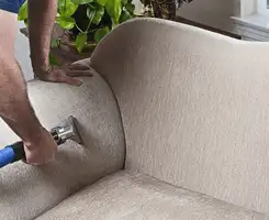 Professional upholstery cleaner deep-cleaning a fabric sofa with a handheld extraction tool and hose in Fort Worth, TX.